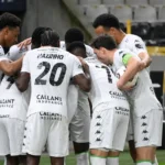 Een groep spelers van Cercle Brugge in witte wedstrijdtenues vormt een huddle op het veld.