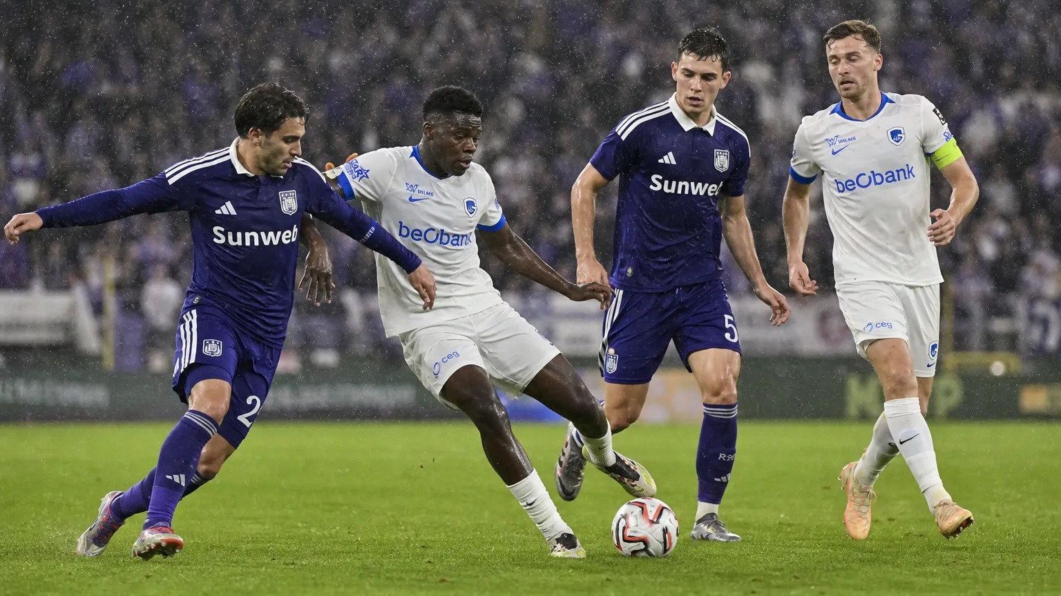 Spelers van Anderlecht en Genk strijden in de regen om de bal.