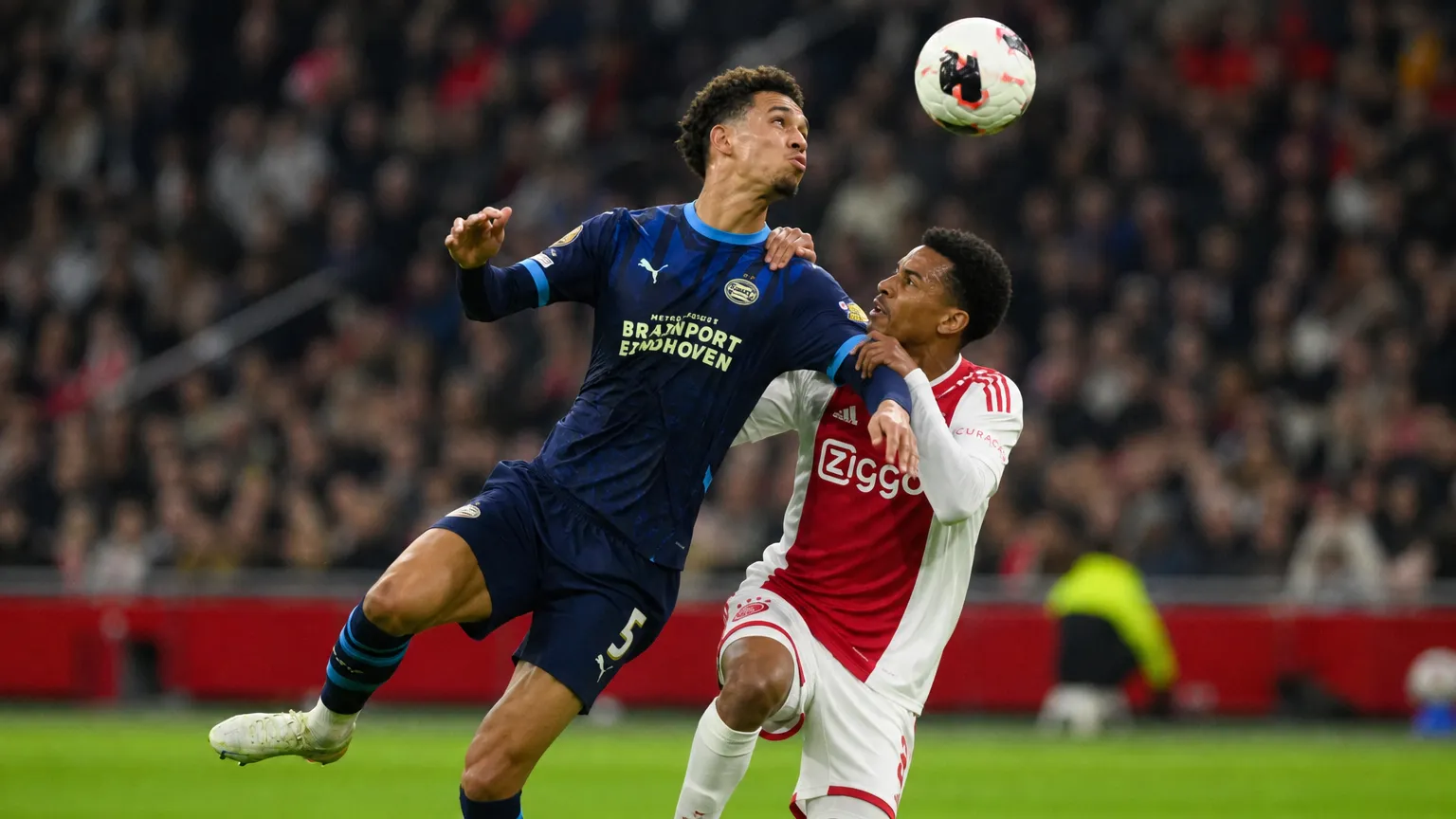 Twee voetballers strijden om de bal tijdens Ajax-PSV.