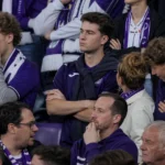 Een groep Anderlecht-supporters met paarse sjaals op de tribune na een wedstrijd.