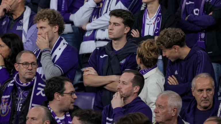 Een groep Anderlecht-supporters met paarse sjaals op de tribune na een wedstrijd.