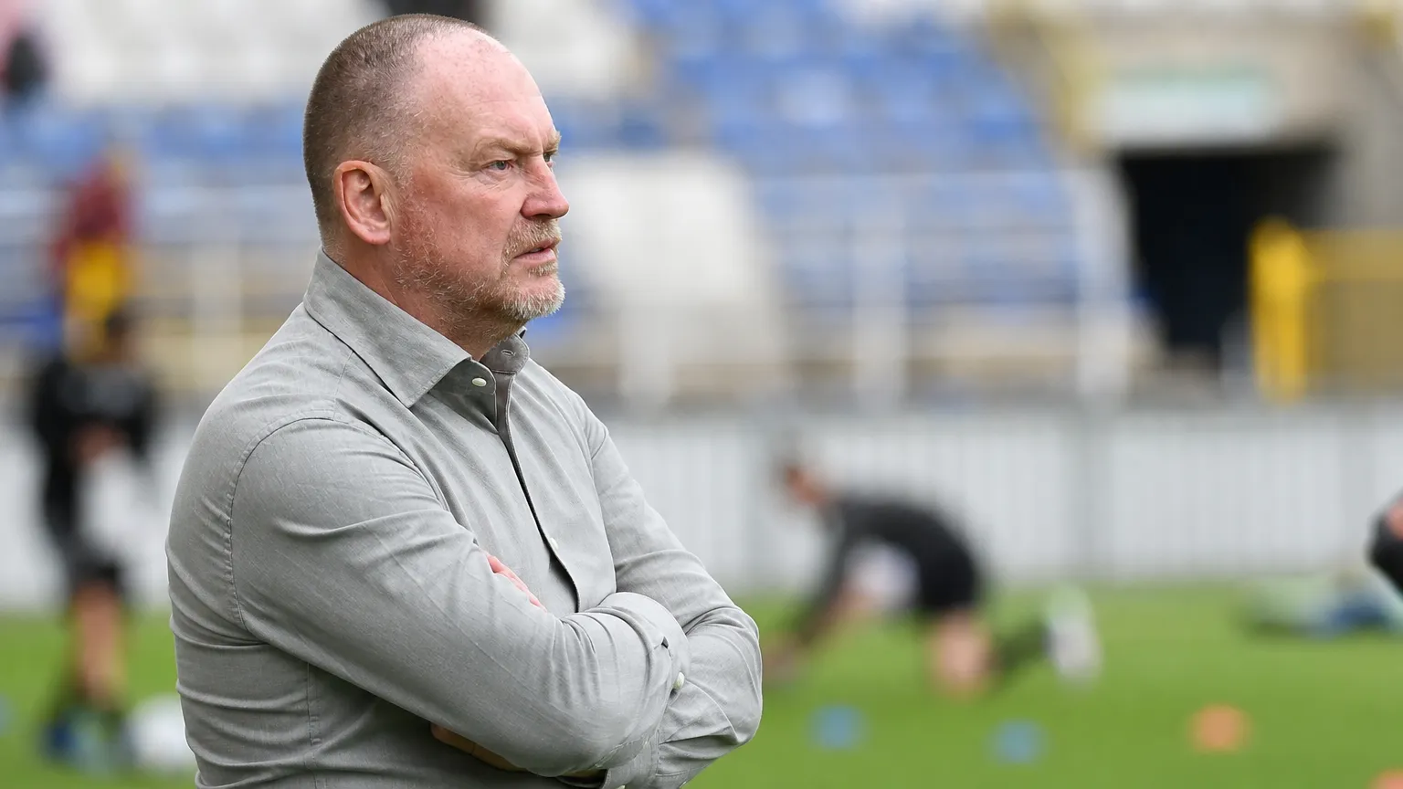 Fred Vanderbiest kijkt geconcentreerd toe vanaf de zijlijn van een voetbalstadion.
