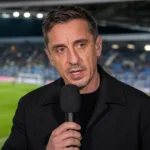 Gary Neville spreekt aan een microfoon bij een overdekte televisiestand langs het veld.