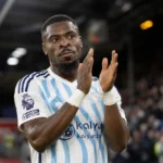 Serge Aurier applaudisseert in een wit shirt met lichtblauwe strepen.