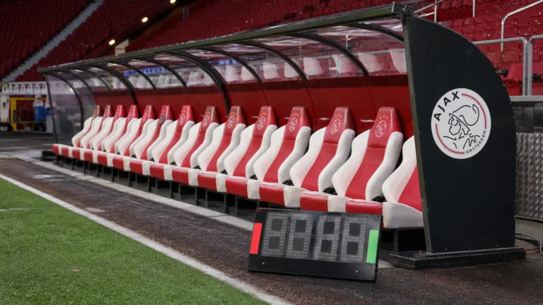 Lege spelersbank van Ajax met een digitaal wisselbord naast het veld.
