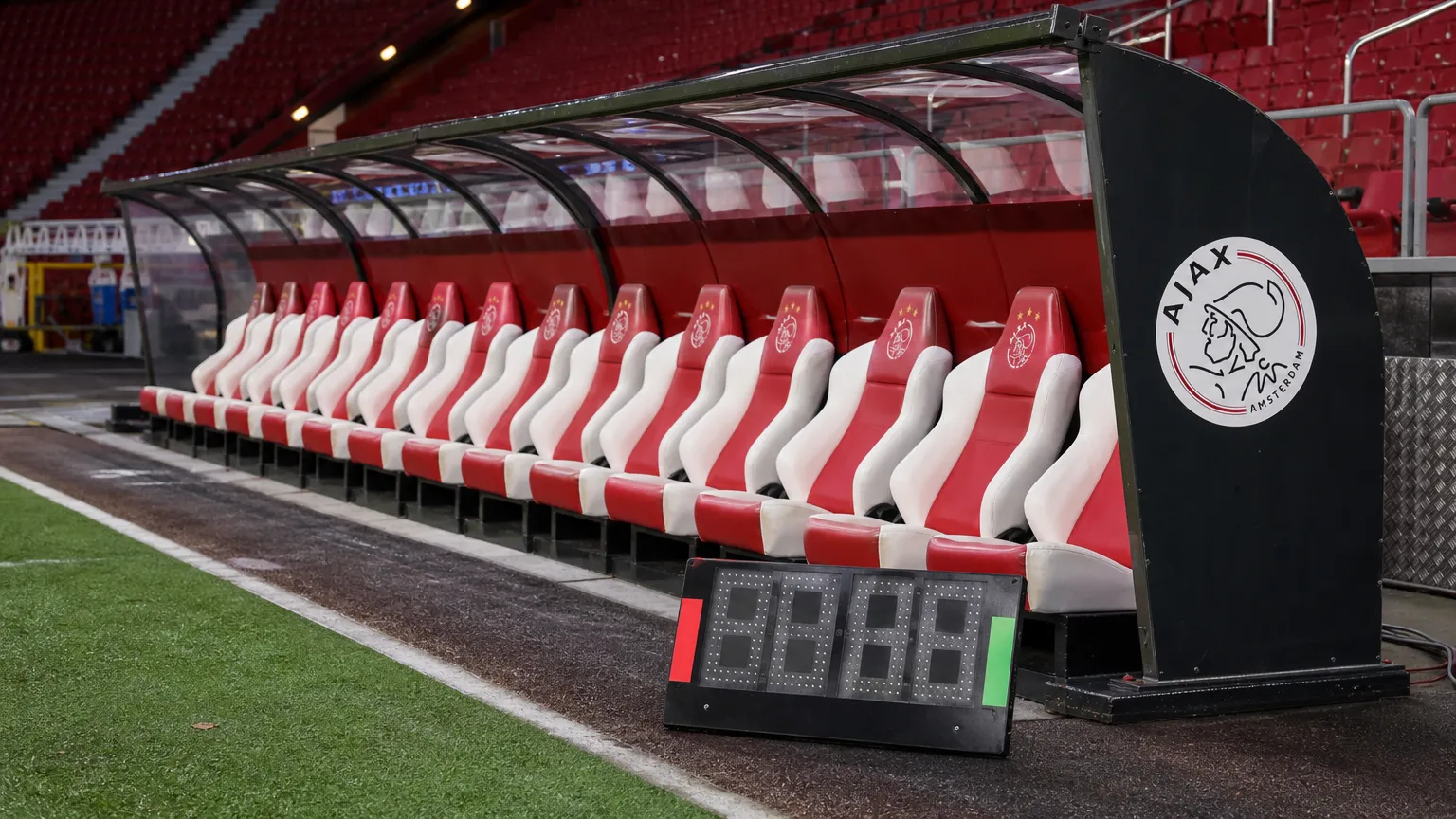 Lege spelersbank van Ajax met een digitaal wisselbord naast het veld.