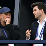 Twee niet-spelende clubvertegenwoordigers in een tribunezone van een stadion.