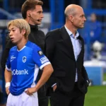 Een speler van KRC Genk en leden van de technische staf aan de zijlijn van een voetbalveld.