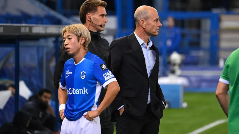 Een speler van KRC Genk en leden van de technische staf aan de zijlijn van een voetbalveld.
