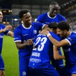 Een groep KAA Gent-spelers viert samen op het veld in blauwe wedstrijdkleding.