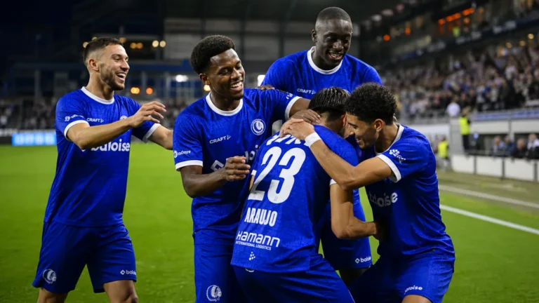 Een groep KAA Gent-spelers viert samen op het veld in blauwe wedstrijdkleding.