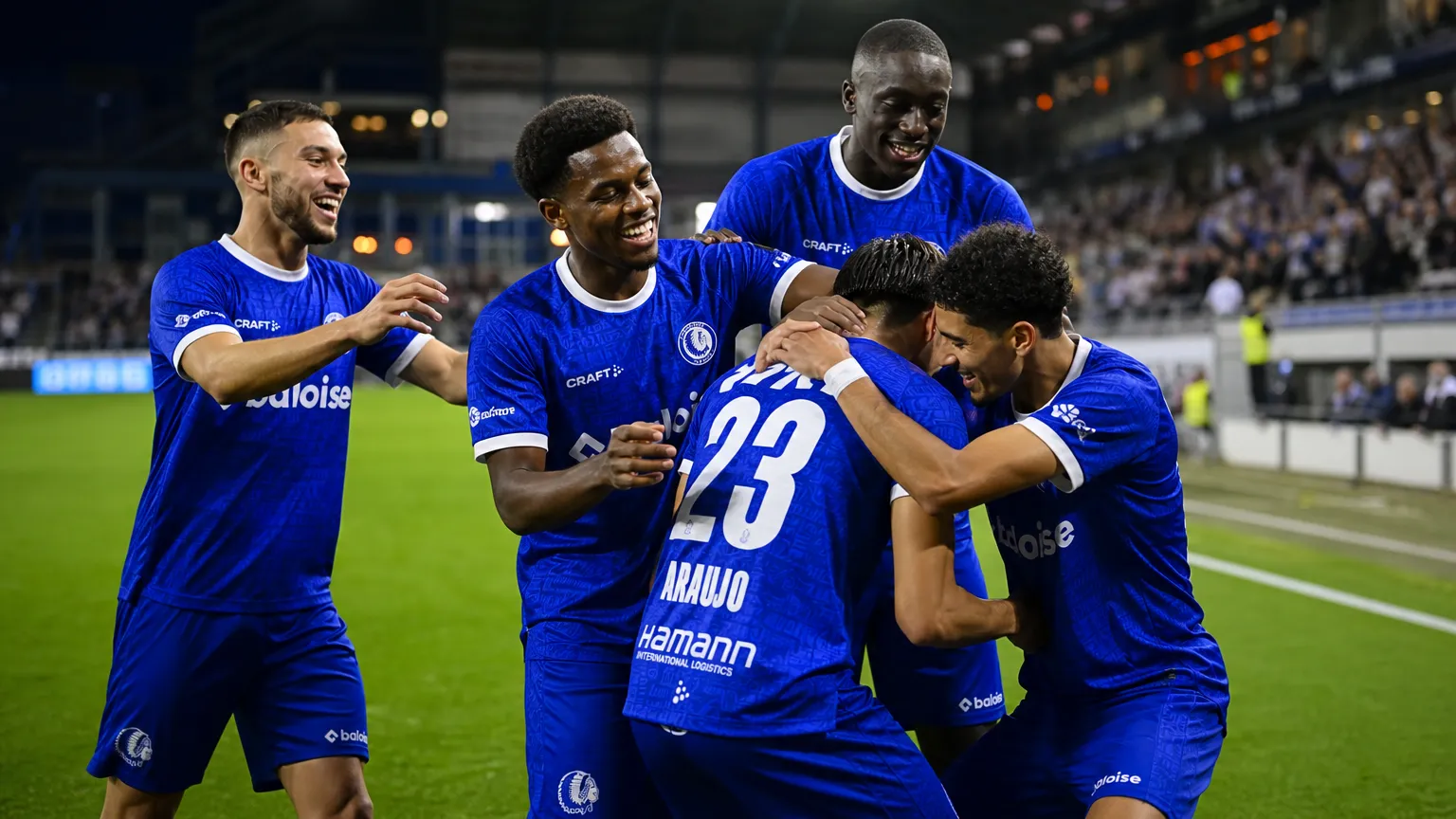 Een groep KAA Gent-spelers viert samen op het veld in blauwe wedstrijdkleding.
