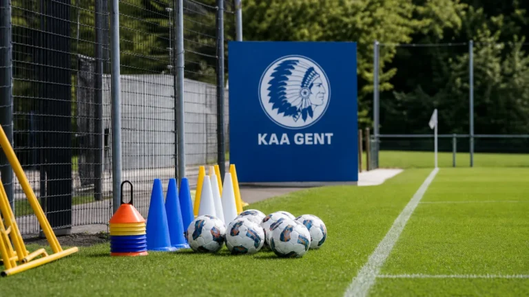 Leeg trainingsveld van KAA Gent met oefenmateriaal langs de zijlijn en een clubembleem op een vast bord.