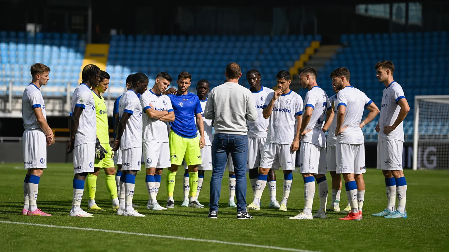 Een spelersgroep in witte tenues verzameld op het voetbalveld.