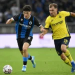 Twee voetballers strijden om de bal op een Belgisch voetbalveld.