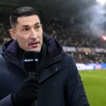 Silvio Proto spreekt tijdens een voetbalinterview in een donkere jas in een stadionomgeving.