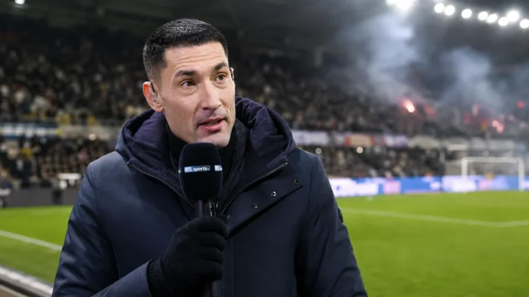 Silvio Proto spreekt tijdens een voetbalinterview in een donkere jas in een stadionomgeving.