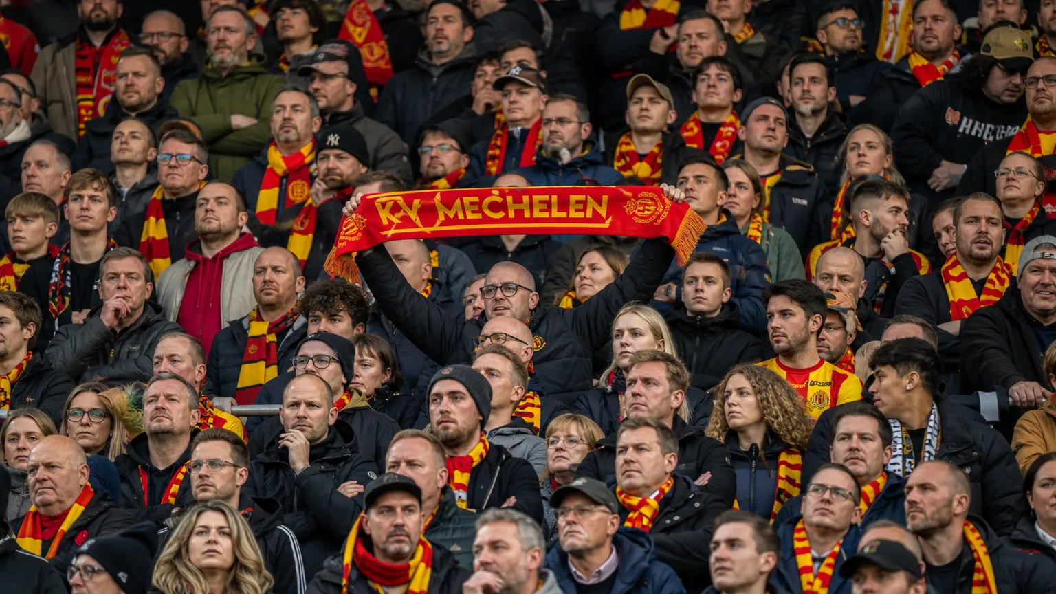 Een dicht opeengepakte groep KV Mechelen-supporters met rood-gele sjaals op de thuistribune.