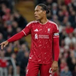Een voetballer in een rood shirt met aanvoerdersband op het veld.