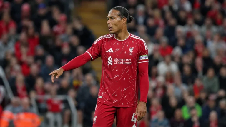 Een voetballer in een rood shirt met aanvoerdersband op het veld.