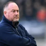 Fred Vanderbiest staat geconcentreerd langs de zijlijn van een voetbalveld.