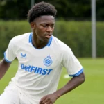 Een jonge speler in een wit shirt met blauwe details op een trainingsveld.