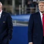 Twee mannen in donkere pakken bij een internationaal voetbalevenement.