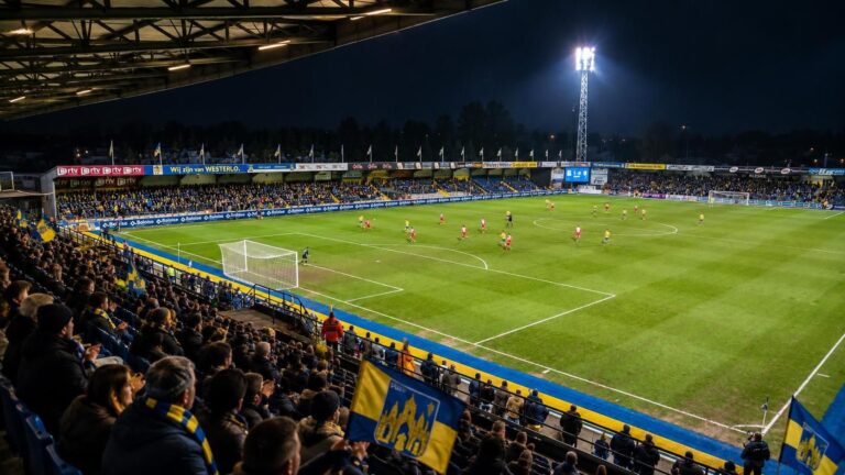 Het compacte ’t Kuipje van KVC Westerlo met het speelveld, overdekte tribunes en geel-blauwe accenten in een Kempense voetbalsfeer.