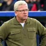 Een niet-spelende stafmedewerker kijkt vanaf de zijlijn naar het veld.