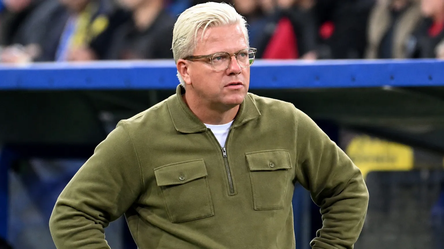 Een niet-spelende stafmedewerker kijkt vanaf de zijlijn naar het veld.