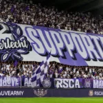 Een volle paars-witte supporterstribune met een groot spandoek.