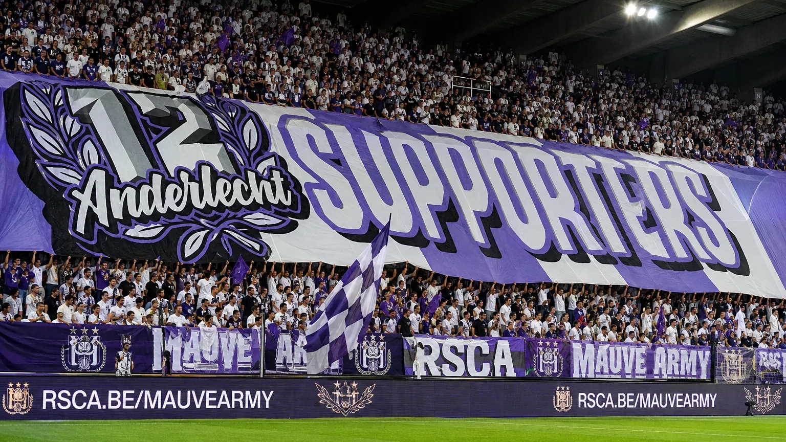 Een volle paars-witte supporterstribune met een groot spandoek.