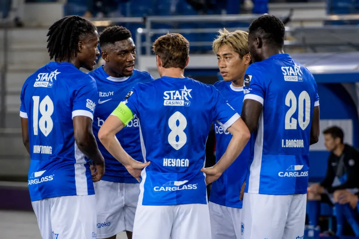 Een groep KRC Genk-spelers in blauwe shirts verzamelt zich rustig langs het veld.