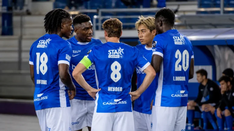 Een groep KRC Genk-spelers in blauwe shirts verzamelt zich rustig langs het veld.