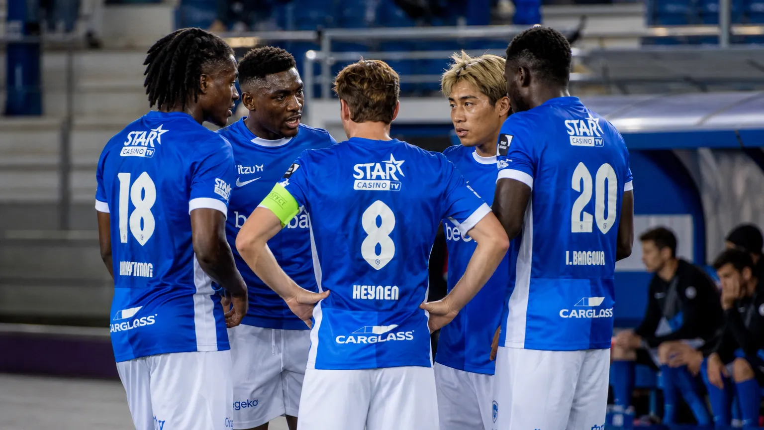 Een groep KRC Genk-spelers in blauwe shirts verzamelt zich rustig langs het veld.