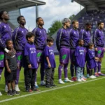Beerschot-spelers in paarse trainingskleding staan met jonge mascottes langs het veld.