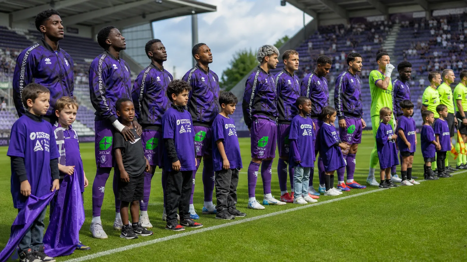 Beerschot-spelers in paarse trainingskleding staan met jonge mascottes langs het veld.