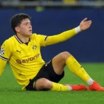 Konstantinos Karetsas zit op het gras in zijn gele wedstrijdtenue tijdens een Champions League-duel.