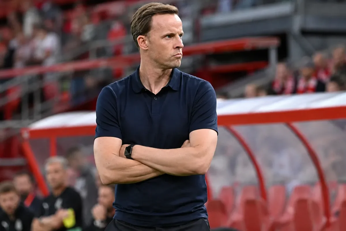 Een Standard-trainer volgt geconcentreerd de wedstrijd vanaf de zijlijn.