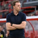 Een Standard-trainer volgt geconcentreerd de wedstrijd vanaf de zijlijn.