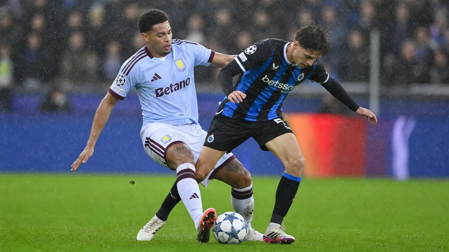 Een speler van Club Brugge in duel met een tegenstander tijdens een regenachtige wedstrijd.