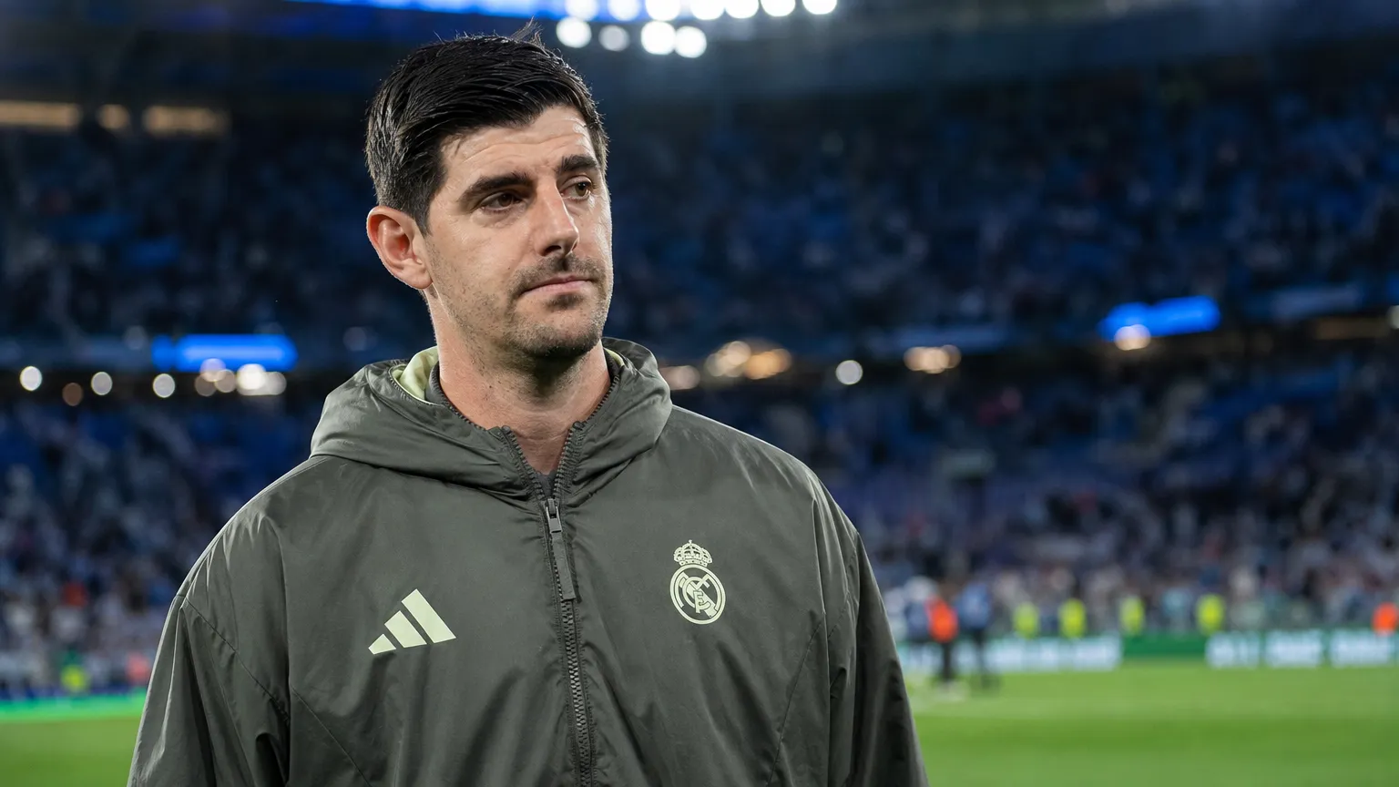 Thibaut Courtois in een donkere Real Madrid-jas aan de rand van het veld na een wedstrijd.