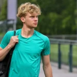 Cedric Hatenboer wandelt met een sporttas langs een trainingsveld.