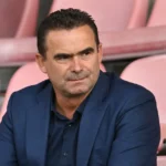 Marc Overmars zit in een rustige stadiontribune in een donkerblauw kostuum.