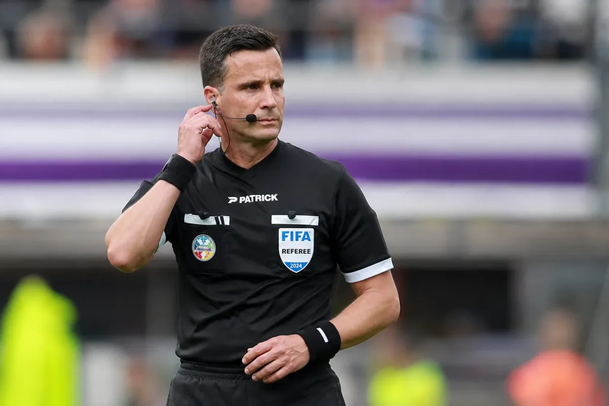 Een scheidsrechter in zwart tenue controleert zijn communicatie voor een wedstrijd in de Jupiler Pro League.