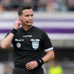 Een scheidsrechter in zwart tenue controleert zijn communicatie voor een wedstrijd in de Jupiler Pro League.