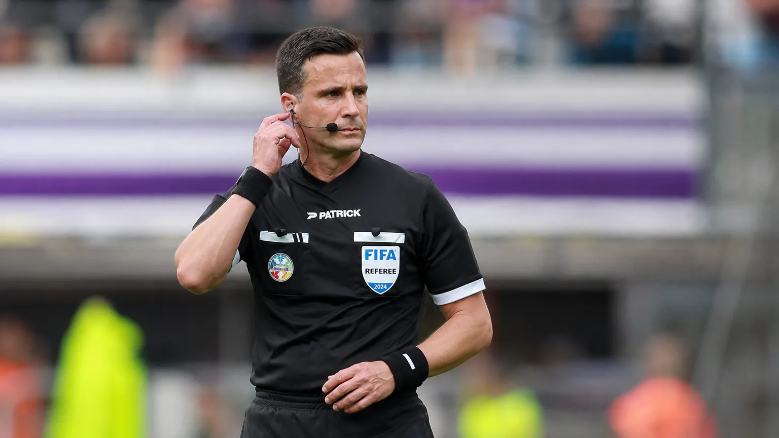 Een scheidsrechter in zwart tenue controleert zijn communicatie voor een wedstrijd in de Jupiler Pro League.