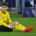 Konstantinos Karetsas zit op het gras in het gele wedstrijdtenue van Borussia Dortmund.