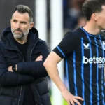 Een lid van de Club Brugge-staf naast spelers in blauw-zwarte shirts langs het veld.