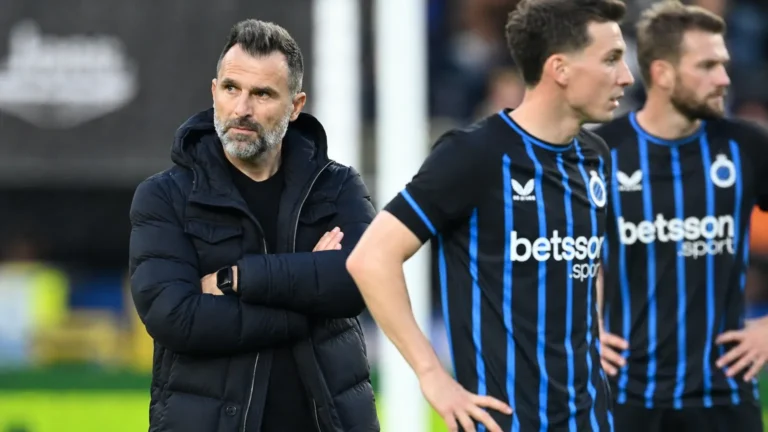 Een lid van de Club Brugge-staf naast spelers in blauw-zwarte shirts langs het veld.